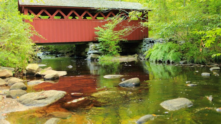 A red covered bridge crosses a gently flowing river in one of Connecticut's stunning state parks.