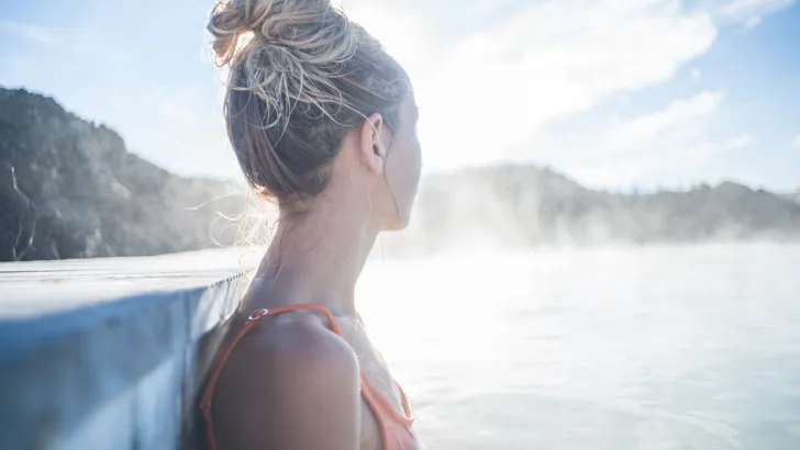 Blonde woman soaking in a hot spring surrounded by mountains, like you might see on your way to Alaska.