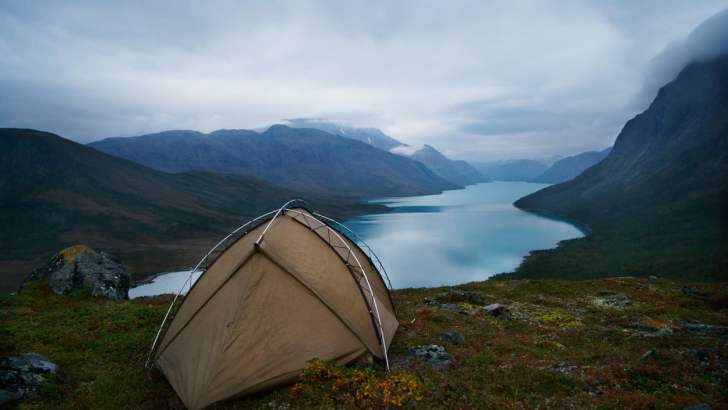 A tent perched high above a crystal-blue lake surrounded by mountains.