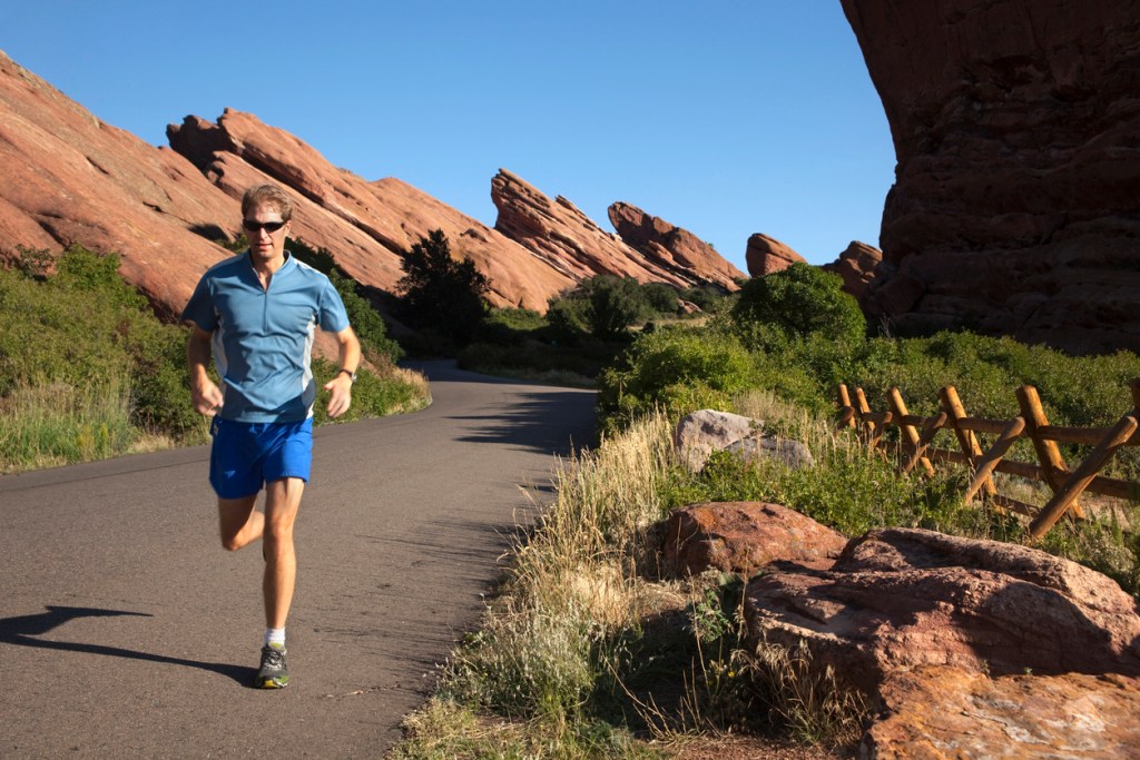 A man in blue jogs through Red Rocks Park, possibly on a day trip from Denver.