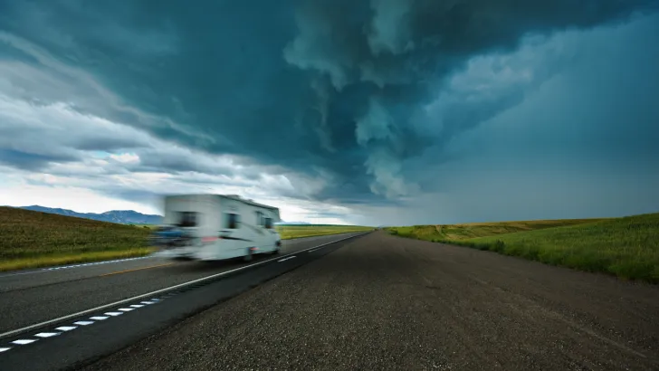 A camper drives down the road toward a rainstorm. Hopefully they've addressed any RV slide leaks!