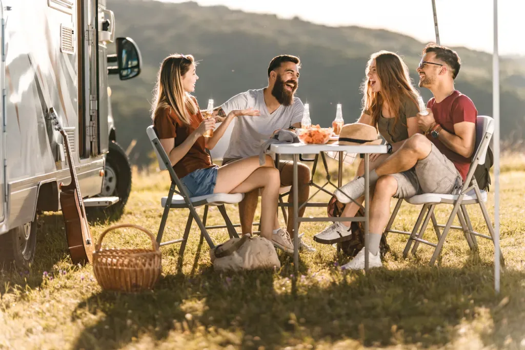 For friends sit around a camp table enjoying snack and drinks.