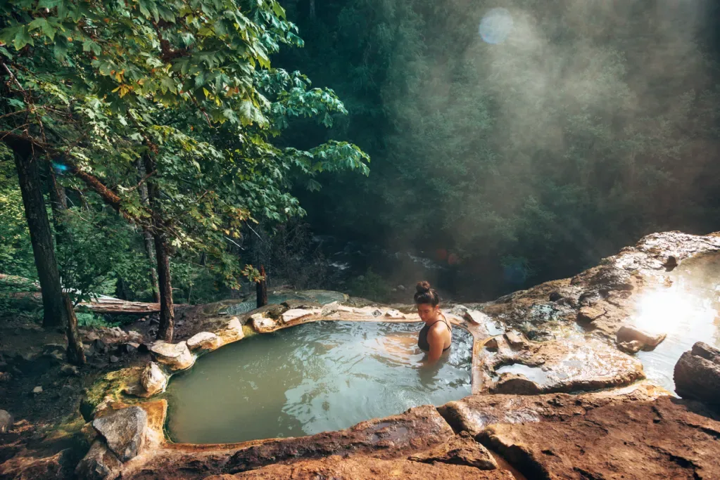 A woman relaxes in a natural mountain-side hot spring like you might see in Washington.
