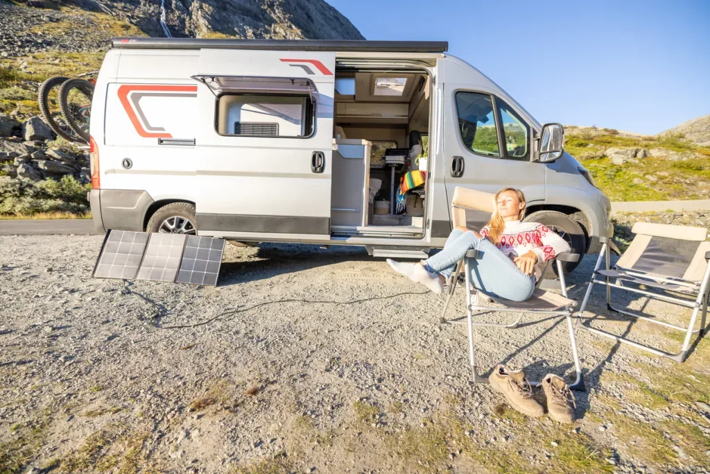 A woman lounging in the sunshine outside of an off-grid Class B.