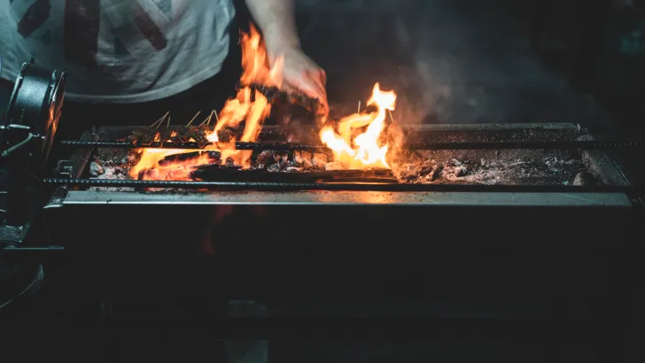 A man cooks over an outdoor grill at night. He could benefit from a rechargeable light!