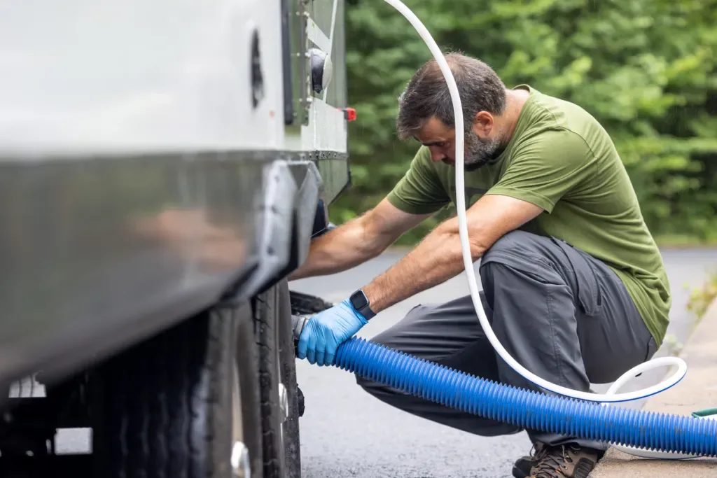 A man hooks up his RV black tank to a sewer line.