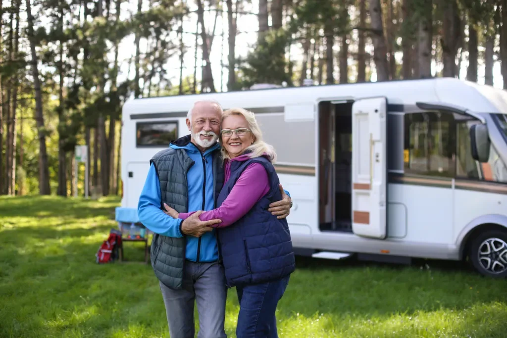 A senior couple embrace outside of a camper in the woods. They may have chosen to rent or buy this RV.