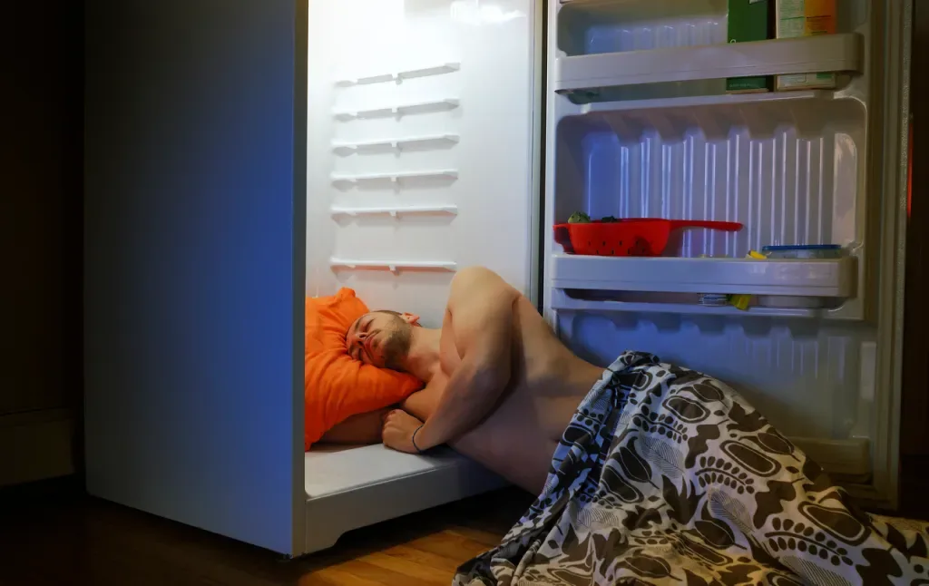 A man sleeps with his head in a refrigerator. A Sweetfull desk fan could cool him down for a much lower cost!