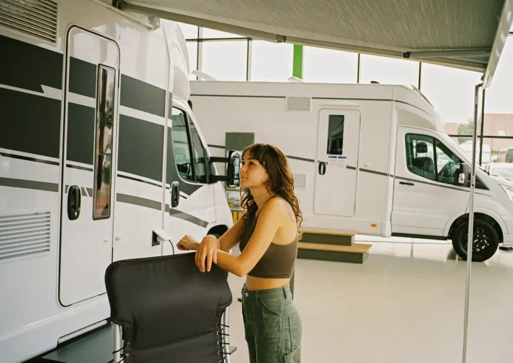 A woman looks at an RV at a dealership, possibly wondering whether to rent or buy.