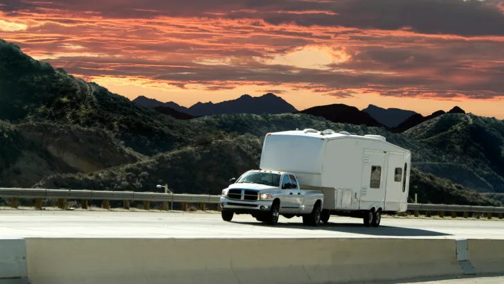 A truck pulls a fifth-wheel RV down the highway at sunset, undoubtedly using a specialized hitch.