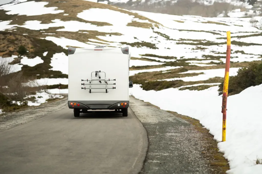 A camper drives through a snowy mountain landscape. Hopefully this RV is equipped with a furnace.
