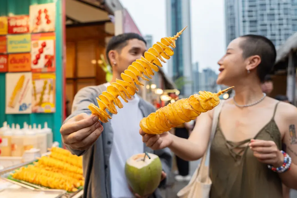 A man and woman enjoy fried, spiraled potatoes at an outdoor food festival, like you might see in Seattle.