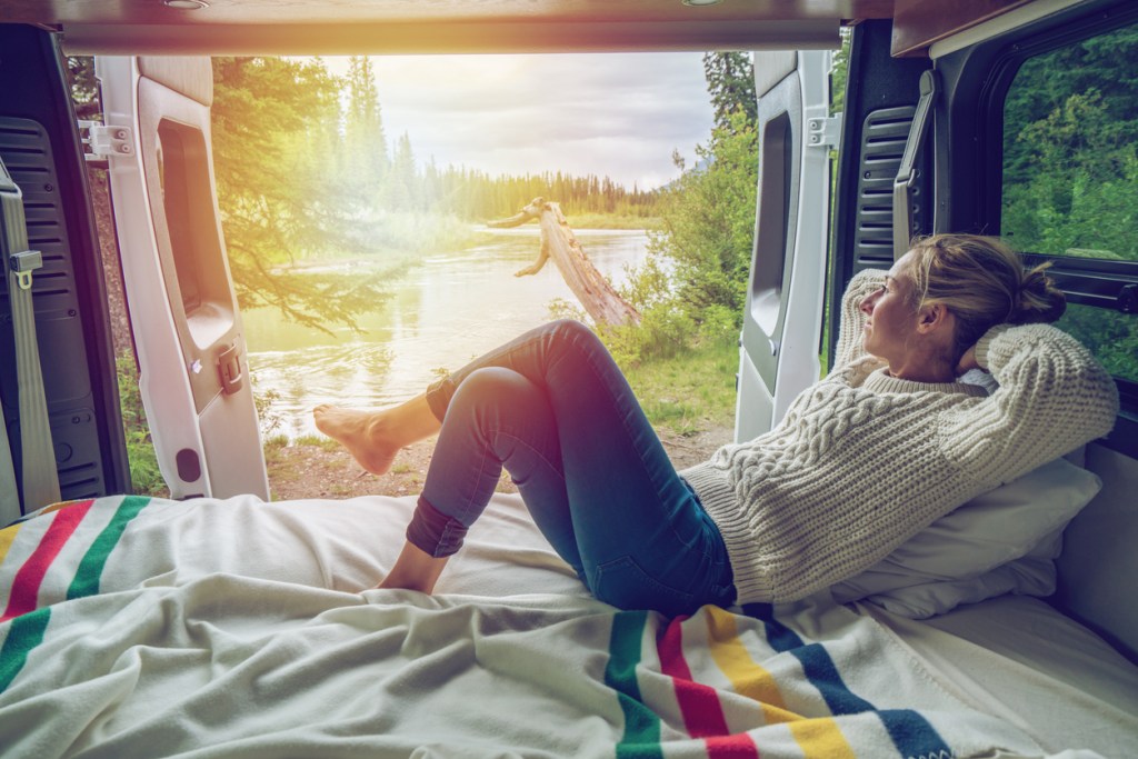 A woman lounges on her RV mattress with the sun setting behind her.