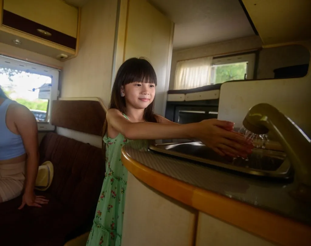 A little girl washes her hands in an RV sink.