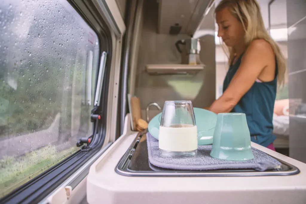 A woman washes dishes in her camper's sink. Hopefully her RV doesn't have improper plumbing.
