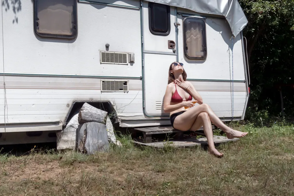 A woman in a swimsuit attempts to cool off outside of an RV.