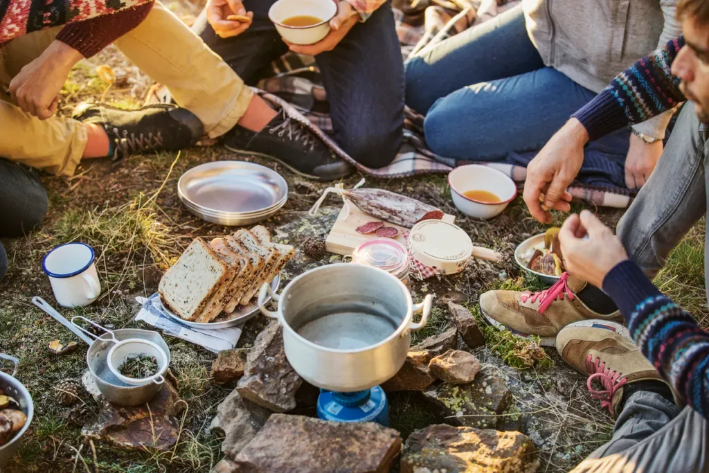 Several friends sit on the ground and enjoy a budget camp meal.