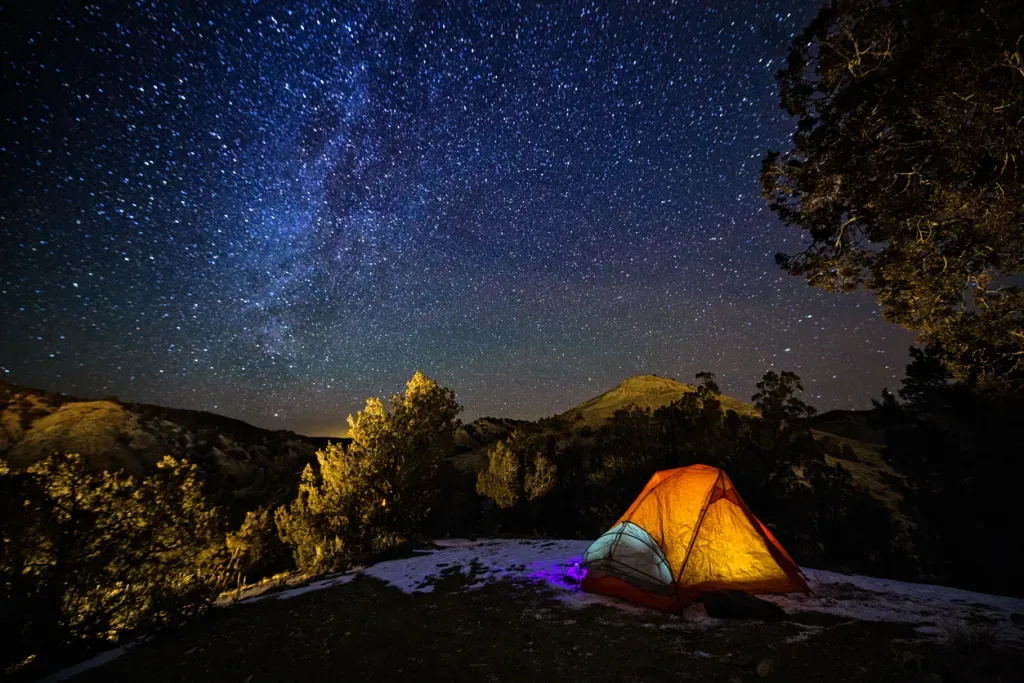 A yellow tent glows under a vast night sky. This is a common occurrence in Colorado's many state parks.