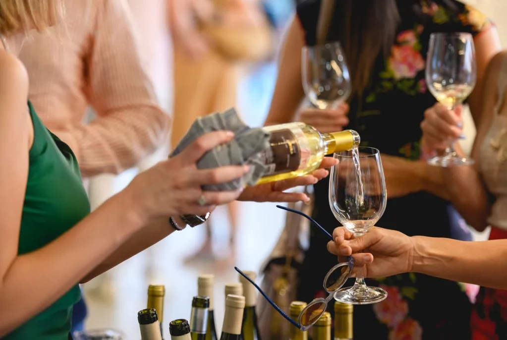 A woman pours wine samples for guests at a tasting event.