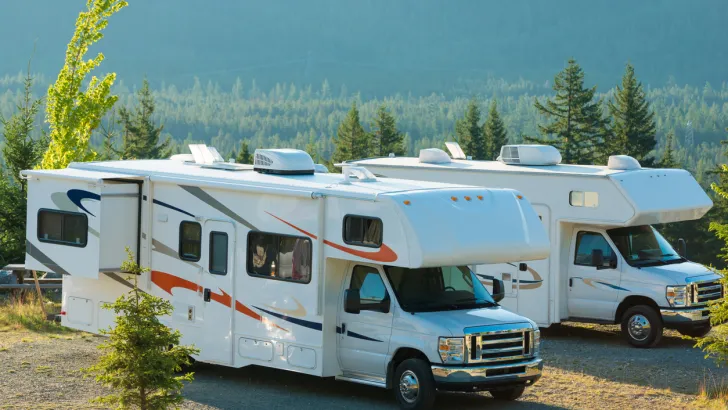 Two Super C RV campers parked side by side in a wooded area.